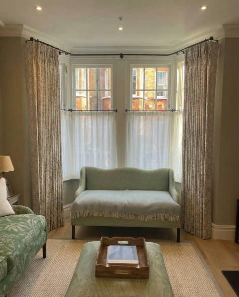 Neutral curtains beside a green sofa